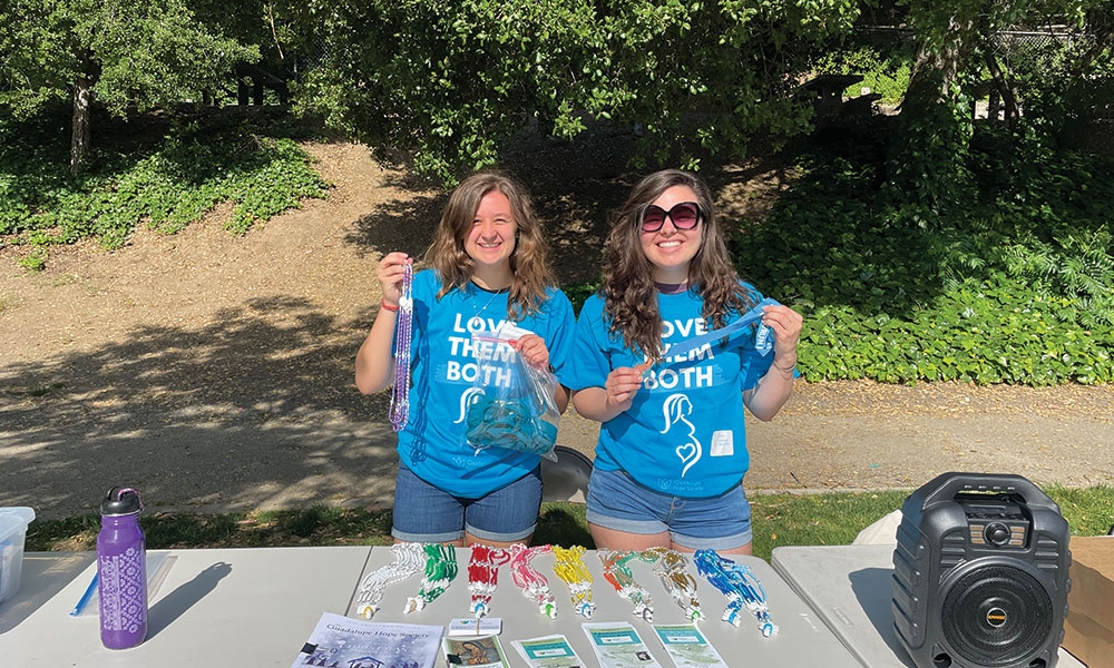 Two Young Adults wearing teal shirts hold up rosaries