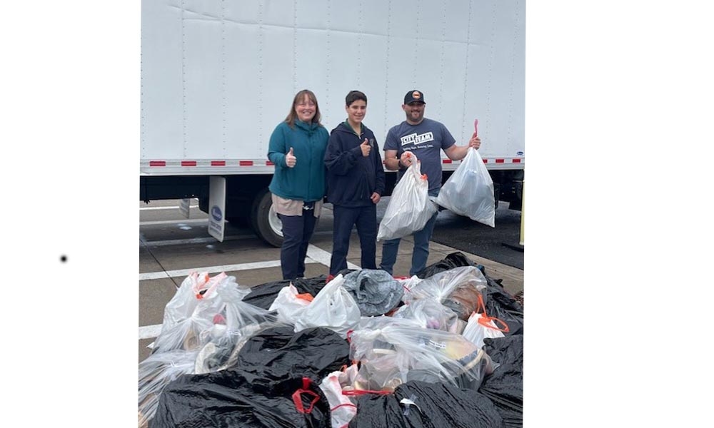 Student stands with adults with bags of donated shoes in front of them