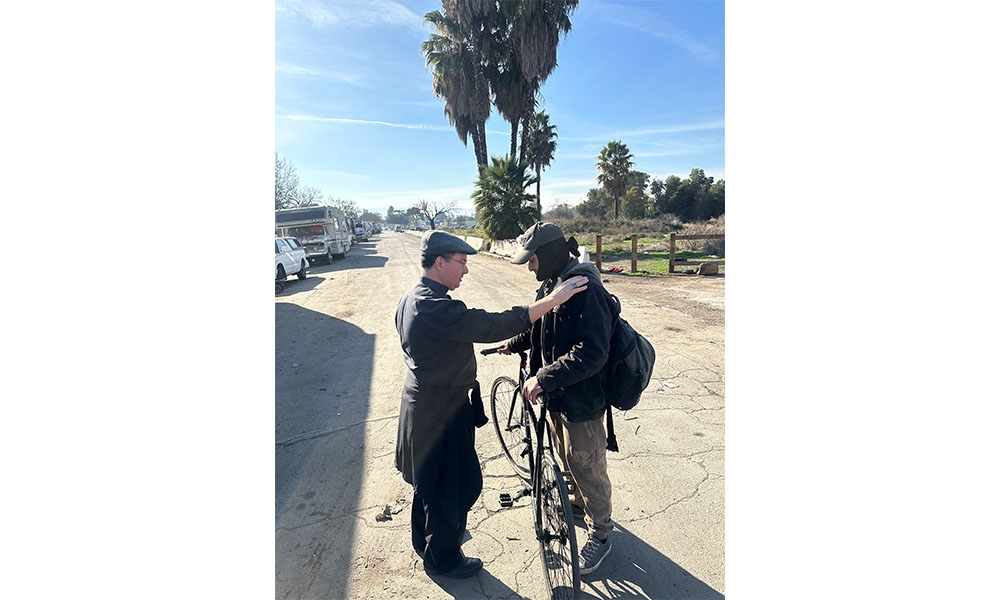 Bishop blesses a homeless man standing next to his bicycle
