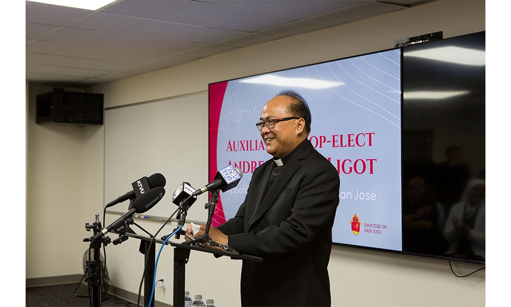 Bishop Elect Andy Speaking at Podium with congrats screen behind him.