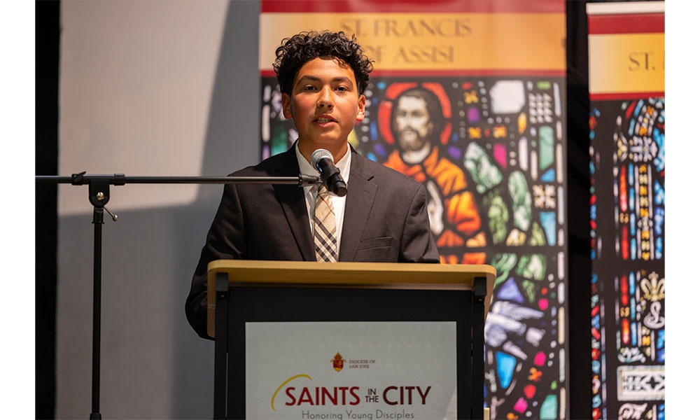 Student stands at podium with saint poster behind him