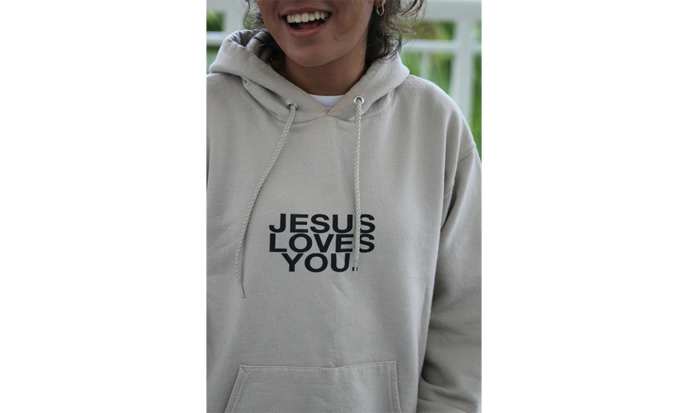 Woman wearing grey hoodie that says "Jesus Loves You"