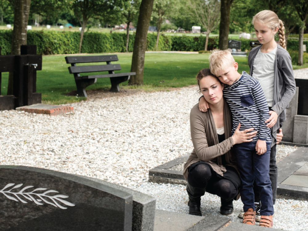 A mother hugs her children by a gravesite